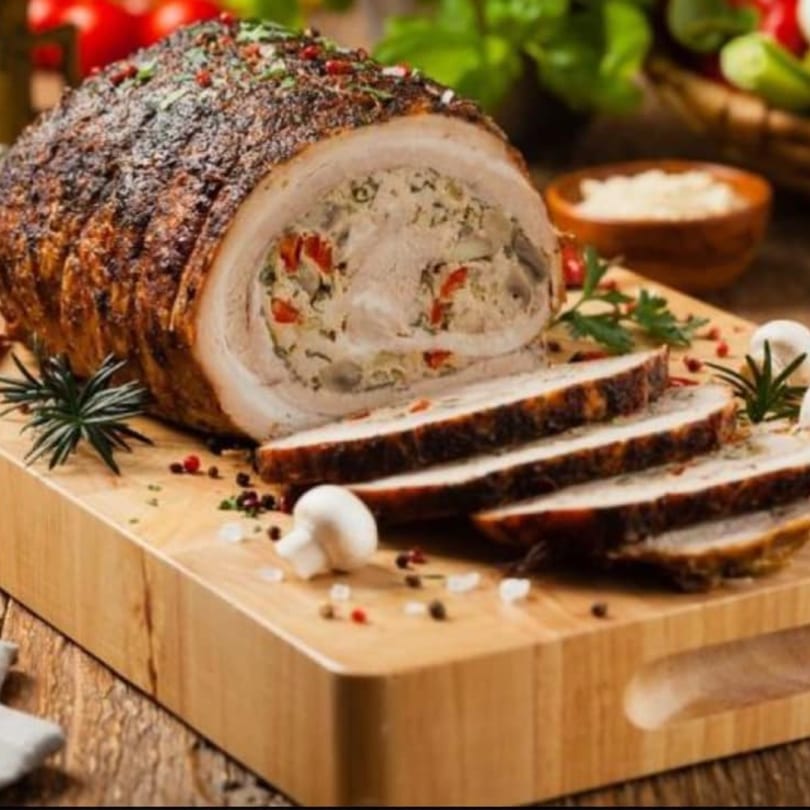 Sliced European stuffed pork roast with herbs and spices on a wooden cutting board.