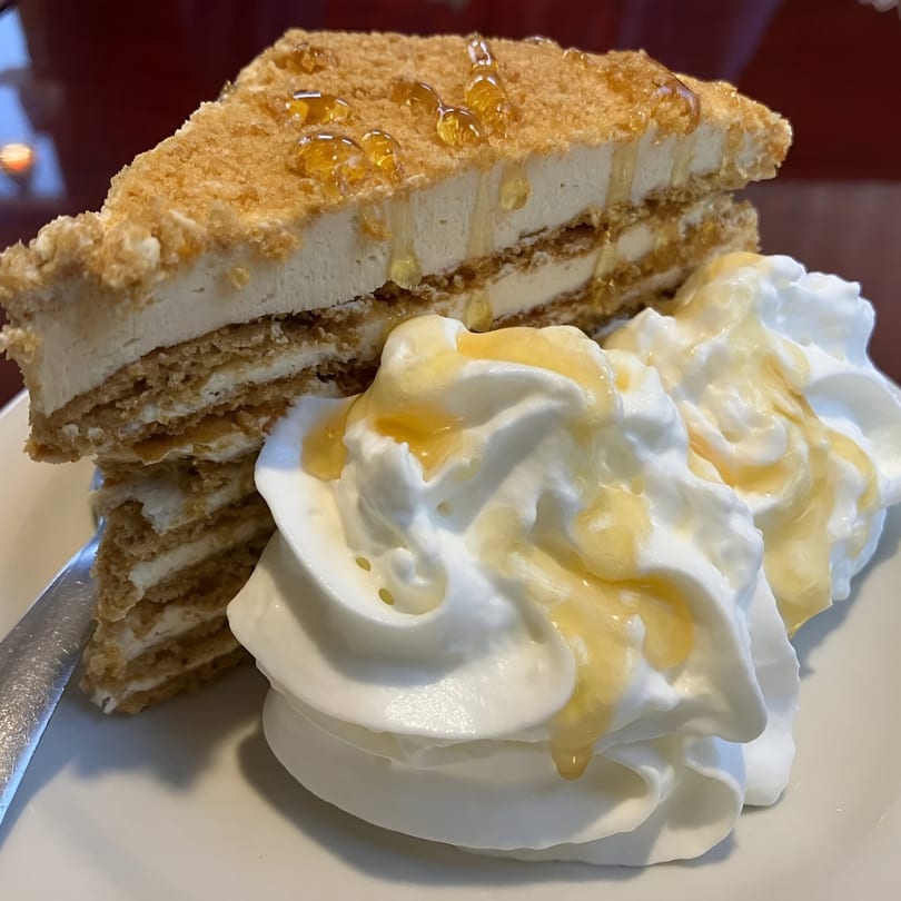 A slice of European honey cake with whipped cream and honey drizzle on a white plate.