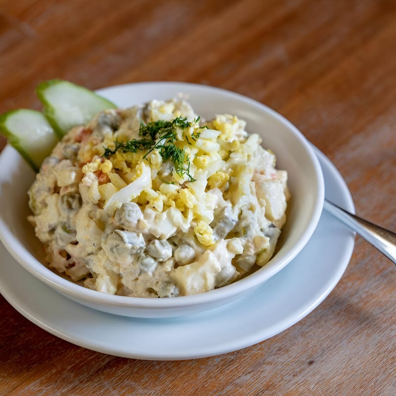 European potato salad with dill, chopped eggs, and cucumber slices in a white bowl.