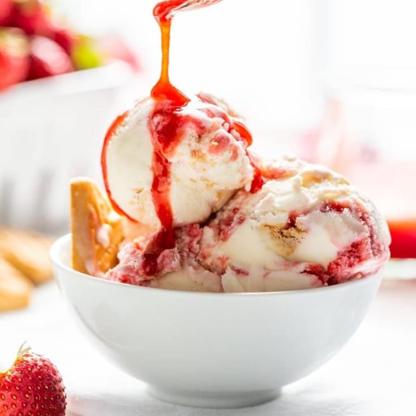 Strawberry ice cream with red syrup being drizzled on top, served in a white bowl.