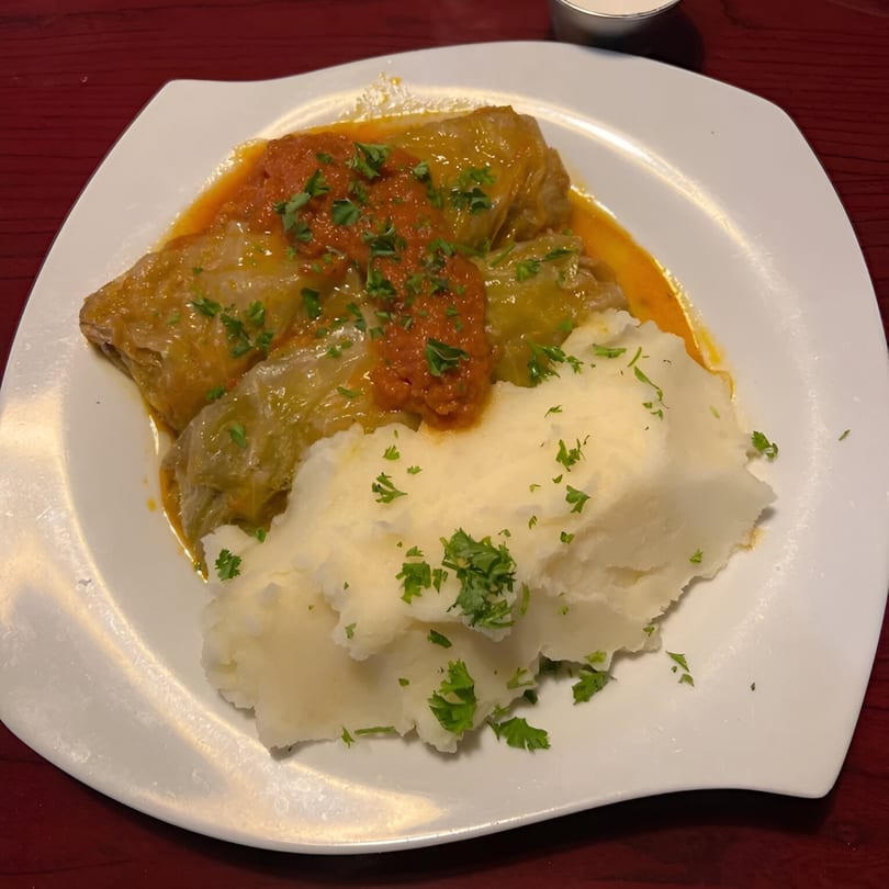 European cabbage rolls with tomato sauce and mashed potatoes, garnished with parsley on a white plate.